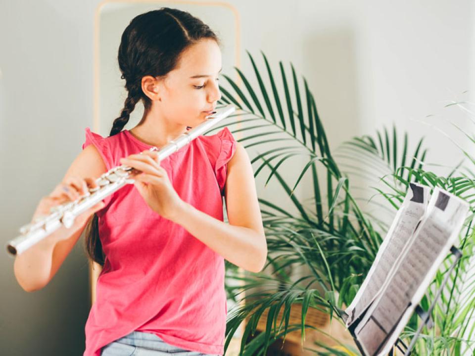 Young teen in pink top plays flute in front of sheet music at home