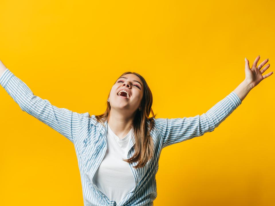 Portrait of young woman with brunette hair looking happy with her hands in the air
