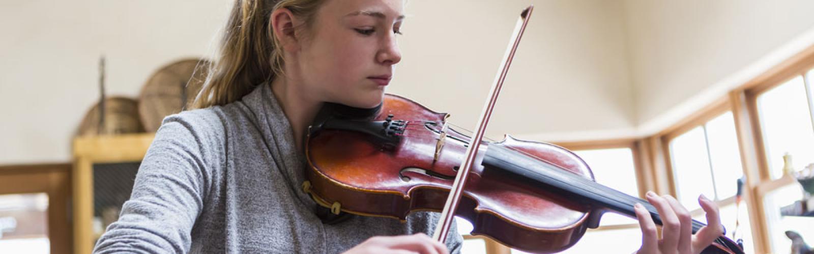 Teen playing violin at home in kitchen 