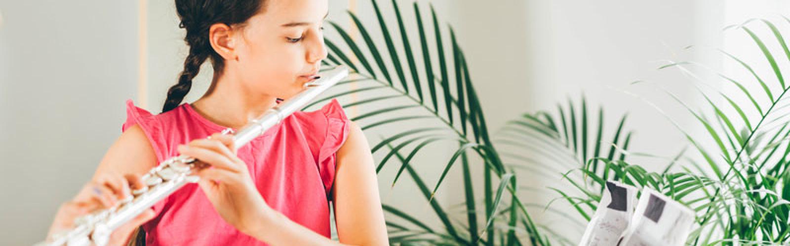 Young teen in pink top plays flute in front of sheet music at home